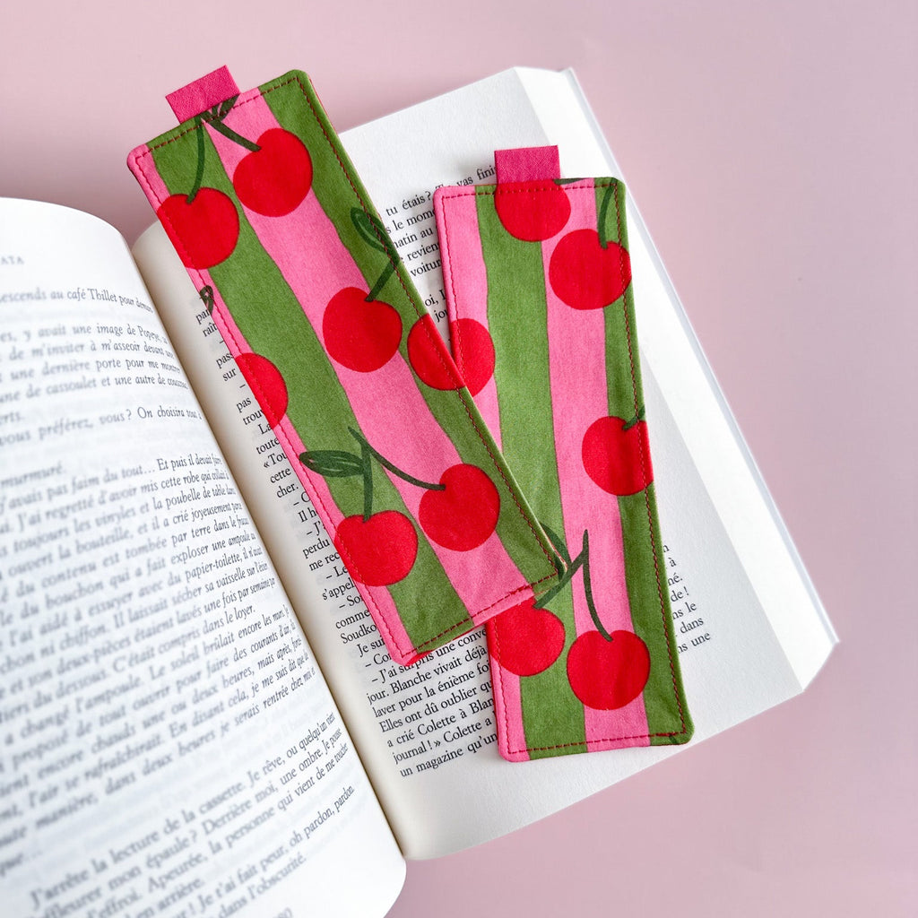 Deux jolis marque-pages en tissu fait main avec un motif de rayures et de grosses cerise rouges posés sur les pages d'un roman.