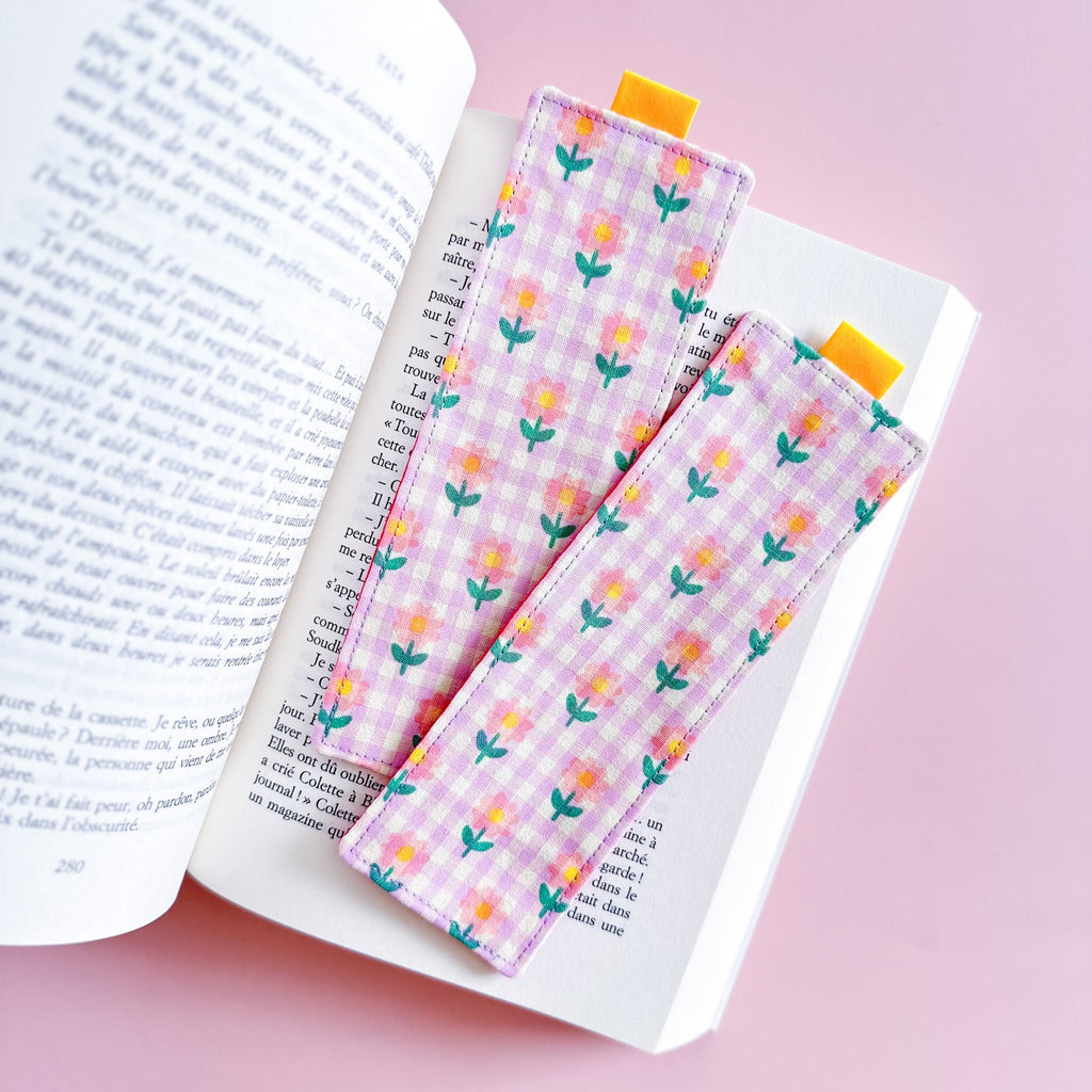 Deux jolis marque-pages en tissu avec motif vichy rose et fleurs pastel, posés sur les pages d'un roman ouvert.