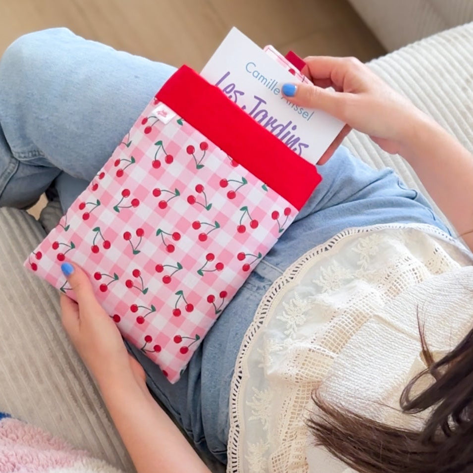 Femme glissant un roman dans une pochette à livre artisanale en coton vichy rose à motifs cerises. Accessoire de lecture fait main.