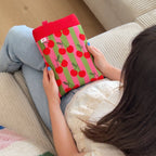 Femme assise tenant une pochette à livre fait main en tissu coton imprimé cerise rouge à rayures rose fuschia et verte. Housse de protection artisanale made in Provence.