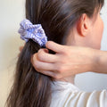 Femme s'attachant les cheveux avec un chouchou à rayures bleues et blanches, accessoire de fabrication artisanale.