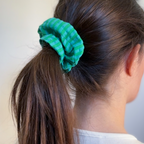 Femme brune aux longs cheveux lisses avec une queue-de-cheval attachée par le chouchou Siena à rayures vertes et bleu turquoise en gaze de coton, accessoire de fabrication artisanale.