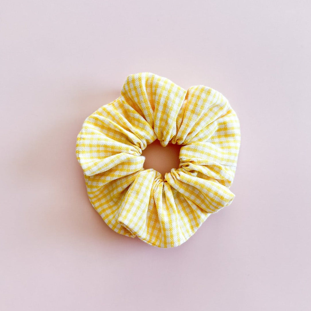 Gros chouchou cheveux Zoé au motif vichy jaune et blanc, accessoire femme de fabrication artisanale de la marque Jolie Myrtille, présenté à plat sur fond rose.