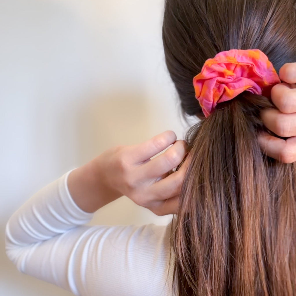 Femme attachant ses cheveux avec le chouchou vichy rose et orange Suzie, création originale de fabrication artisanale pour une coiffure estivale et colorée.