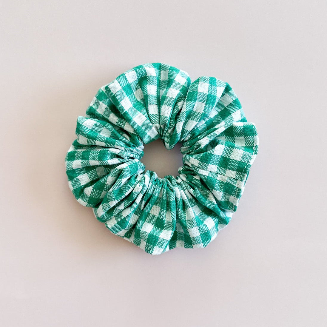 Gros chouchou cheveux Francine au motif vichy vert émeraude et blanc, accessoire femme de fabrication artisanale de la marque Jolie Myrtille, présenté à plat sur fond rose pastel.