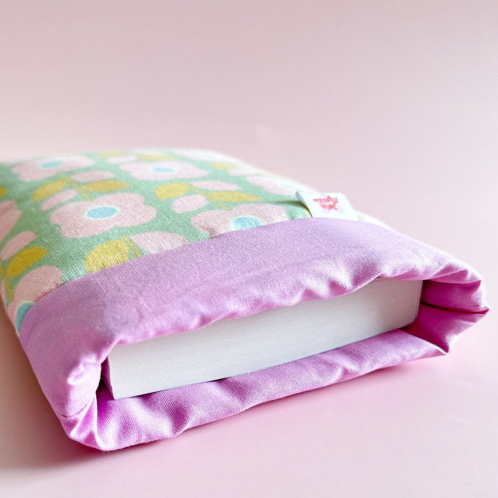 Détail de l'ouverture d'une housse de protection pour livre montrant l'épaisseur du molletonnage avec un livre à l'intérieur. Motif floral et bordure mauve.
