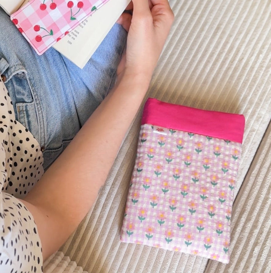 Lectrice assise avec un livre ouvert sur les genoux, protégée par sa housse à livre en tissu rose fleuri fait main.