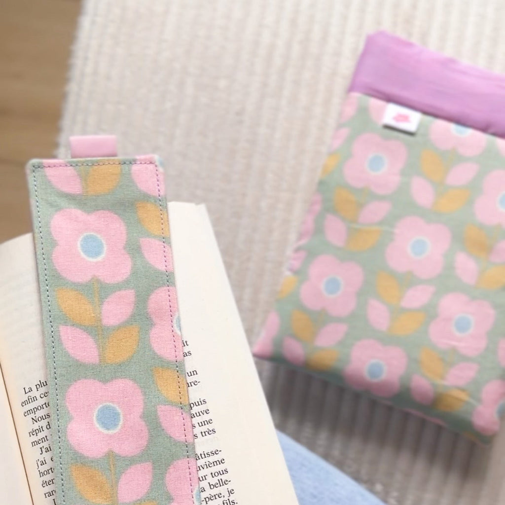 Zoom sur un marque-page en tissu fait main aux motifs floraux vert et rose, délicatement posé sur un livre ouvert à côté de sa pochette de lecture assortie.
