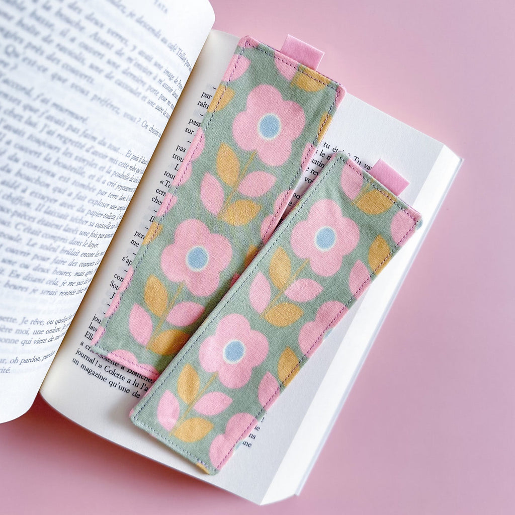 Deux jolis marque-pages en tissu fait main avec des motifs de fleurs roses et bleues, posés sur les pages d'un roman.