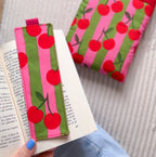 Marque-page en tissu fait main motif rayures roses et vertes avec cerises, posé sur un livre avec sa pochette à livre assortie en arrière plan.