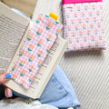 Marque-page fait main en tissu vichy rose à petites fleurs posé sur un livre avec sa pochette de lecture assortie en arrière plan.