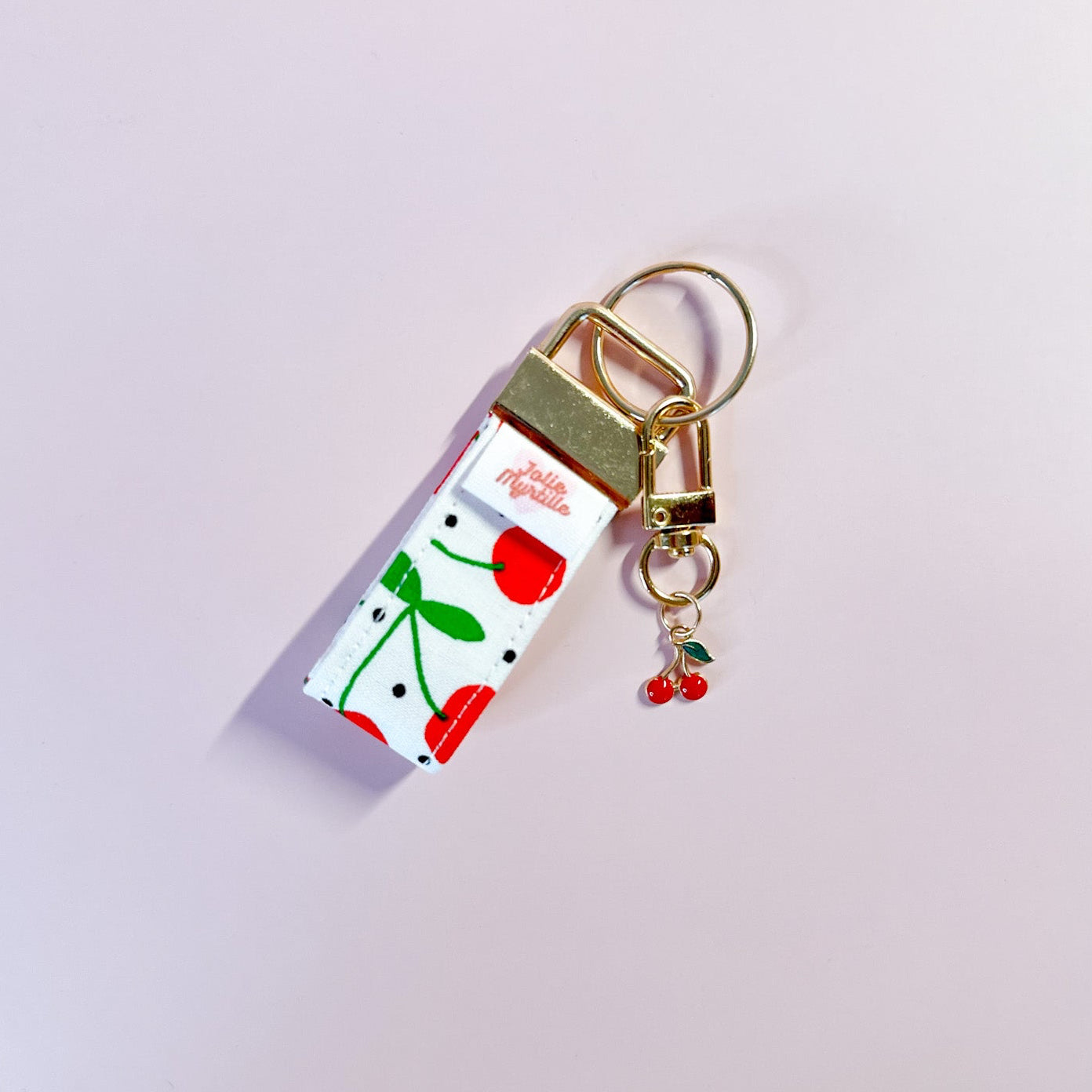 Bijou de sac et porte-clés Griotte posé à plat sur fond rose, accessoire fait main coloré avec sa boucle dorée.