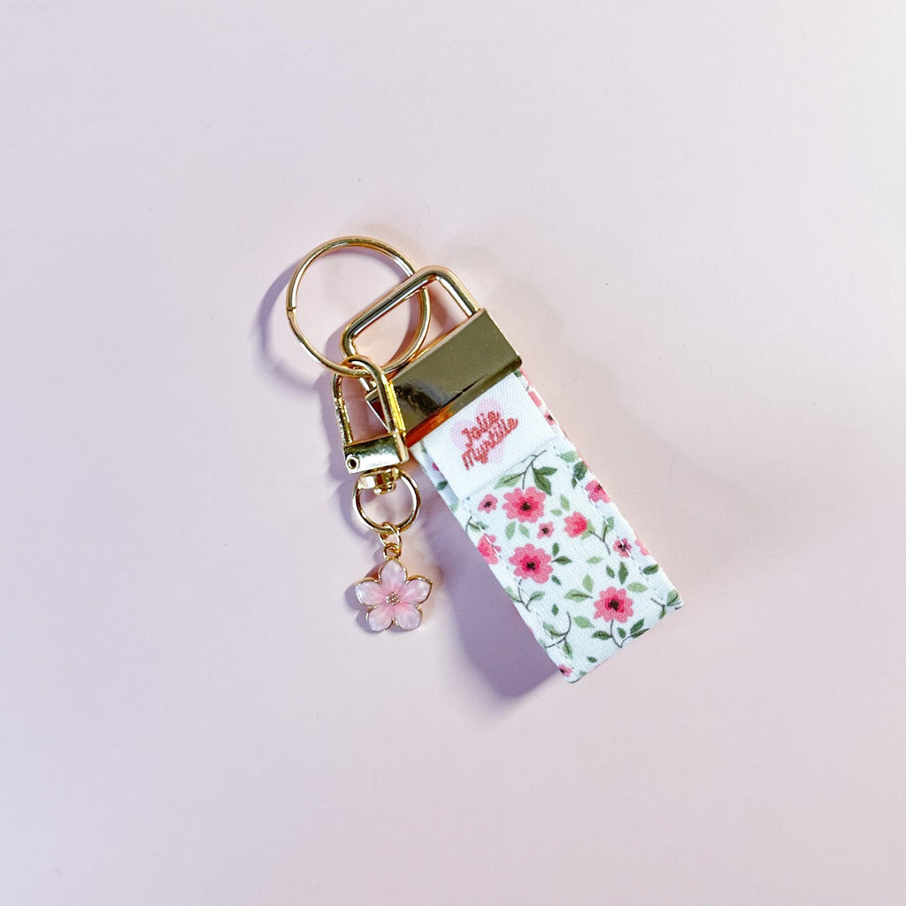 Bijou de sac et porte-clés Anita en tissu motif fleurs posé à plat sur fond rose, accessoire fait main avec sa boucle dorée et sa breloque fleur.