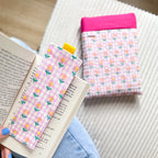 Ensemble de lecture comprenant une pochette à livre et un marque-page en tissu assorti, motif petites fleurs roses, posés à côté d'un livre ouvert.