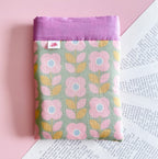 Vue de face d'une pochette pour livre en tissu à motif de grandes fleurs roses sur fond vert, rehaussée d'un bandeau mauve uni sur le dessus.
