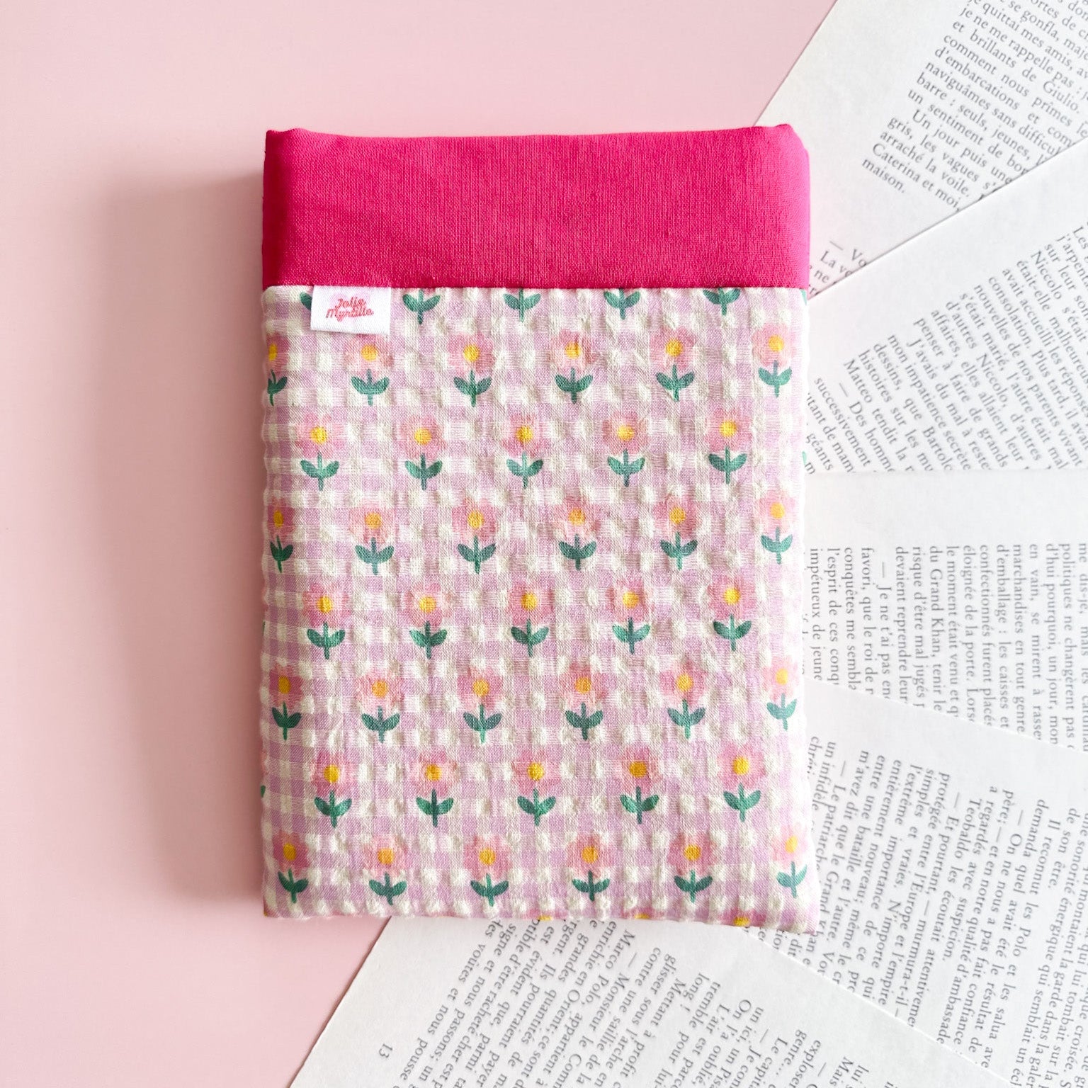 Vue de face d'une pochette pour livre de poche en tissu matelassé, motif fleurs roses avec un bord rose fuchsia uni.