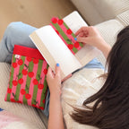 femme assise tenant un livre dans ses mains avec un marque pages en tissu cousu main et une pochette à livre imprimés cerise rouge à rayures rose et verte.