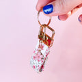Main tenant le mini porte-clés Anita en tissu motif fleuri, montrant le mousqueton doré et son charm fleur rose. Produit fait main.