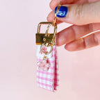 Main tenant le mini porte-clés Rosie en tissu vichy rose et blanc, montrant le mousqueton doré et son petit charm fleur rose. Produit fait main.