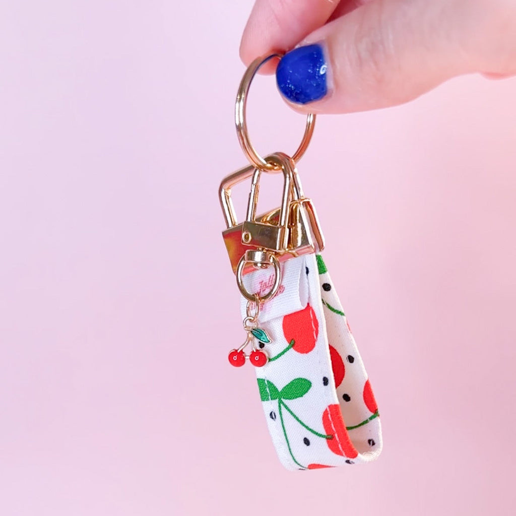 Main tenant un mini porte-clés en tissu fait main avec motif cerises et pois, montrant le mousqueton doré et son charm cerise.