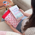 Housse pour livre en tissu vichy rose cerise posée sur les genoux d'une lectrice. Protection de livre en tissu cousu main.