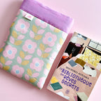 Protège-livre en tissu fleuri et coloré présenté à côté du roman La Bibliothèque des rêves secrets, l'accessoire indispensable pour voyager l'esprit léger.